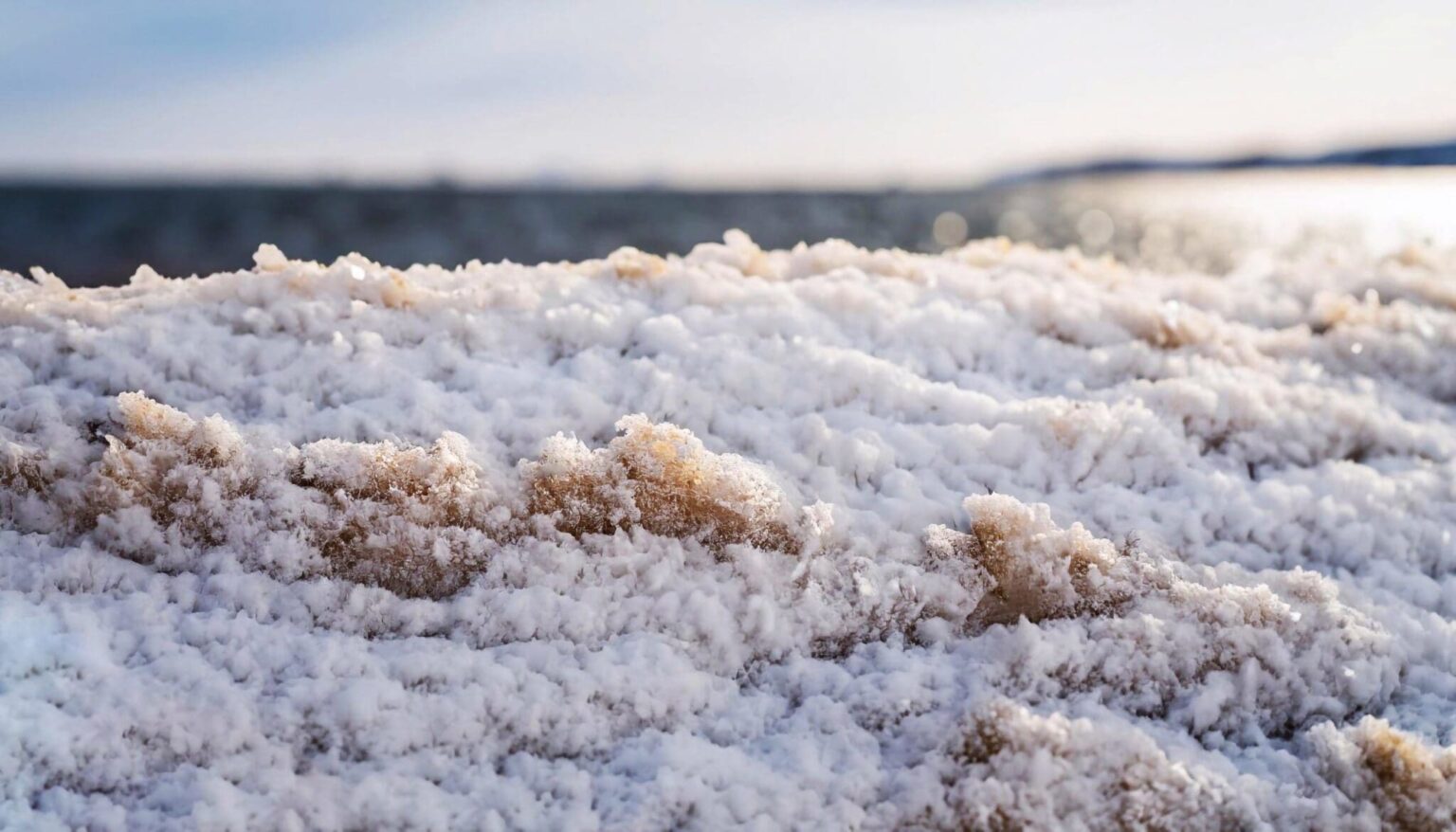 Chunks icy snow along sandy beach that is mostly snow covered winter day